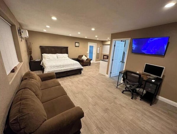 A bedroom with a bed, a brown sofa, a desk with a computer, and a TV on the wall.