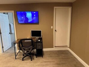 A room with a wooden desk, a computer, a chair, and a television mounted on the wall.