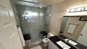 Ein modernes Badezimmer mit Duschkabine aus Glas, einer weißen Toilette, einem schwarzen Waschtisch und einem Spiegel mit Beleuchtung darüber.