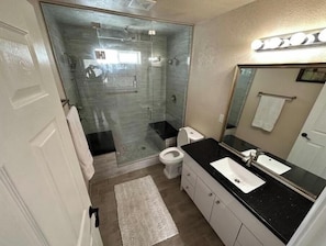 A modern bathroom with a glass shower enclosure, a white toilet, a black countertop sink, and a mirror with lights above it.