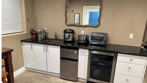 Eine kompakte Küche mit weißen Schränken, einer schwarzen Arbeitsplatte, einer Kaffeemaschine, einem Toaster und einer Mikrowelle.