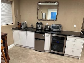 A compact kitchen with white cabinets, a black countertop, a coffee maker, a toaster, and a microwave.
