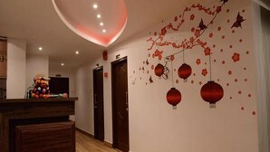 Eine Hotelhalle mit Holzboden, einer Rezeption und einer Wand, die mit roten Laternen und floralen Mustern verziert ist.