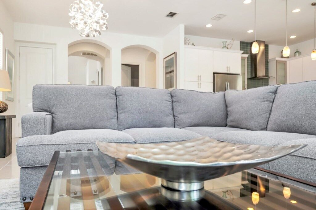 Ein modernes Wohnzimmer mit einem grauen Ecksofa, einem Glastisch und einer Chandelier.