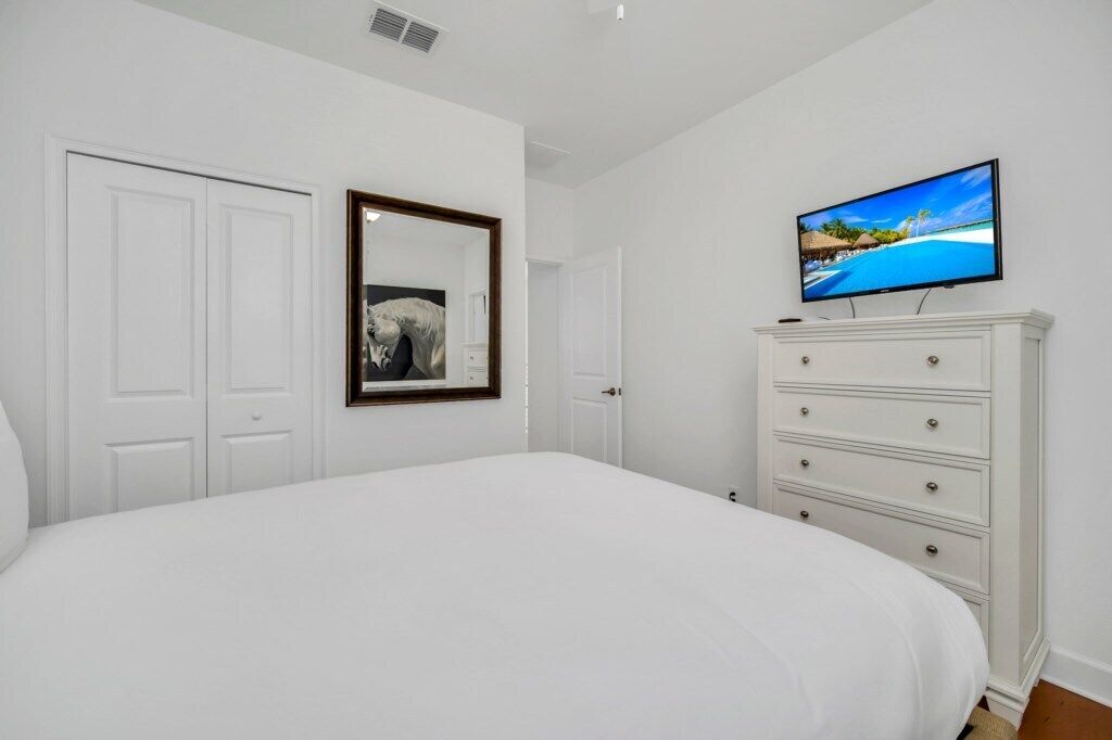 A bedroom with a large bed, a dresser, a television on the wall, and a mirror.