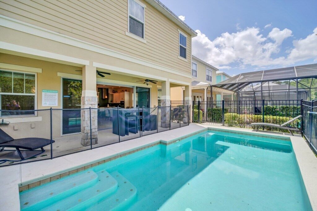 A pool area with a covered patio, lounge chairs, and a clear sky.