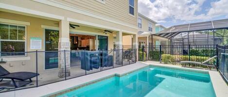 A pool area with a covered patio, lounge chairs, and a clear sky.