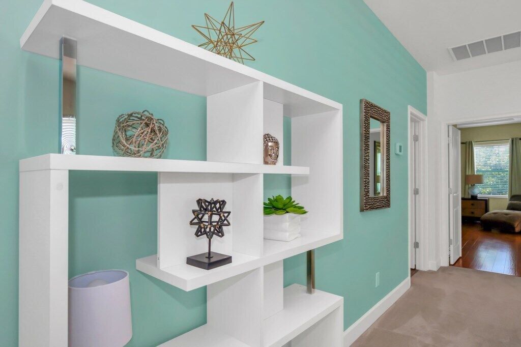 A hallway with white shelving units against a teal wall, each shelf holding decorative items and a potted plant.