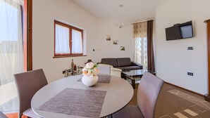 A modern living room with a round dining table, two chairs, a sofa, a TV mounted on the wall, and a window with curtains. - Lovely apartment in Pula with WiFi (Pula)