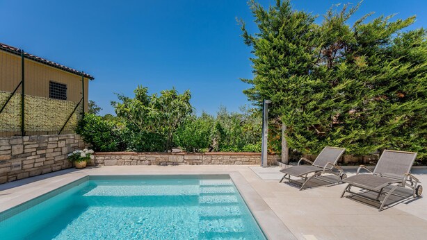 A swimming pool with lounge chairs, a stone wall, and a building with a tiled roof. - Lovely apartment in Pula with WiFi (Pula)
