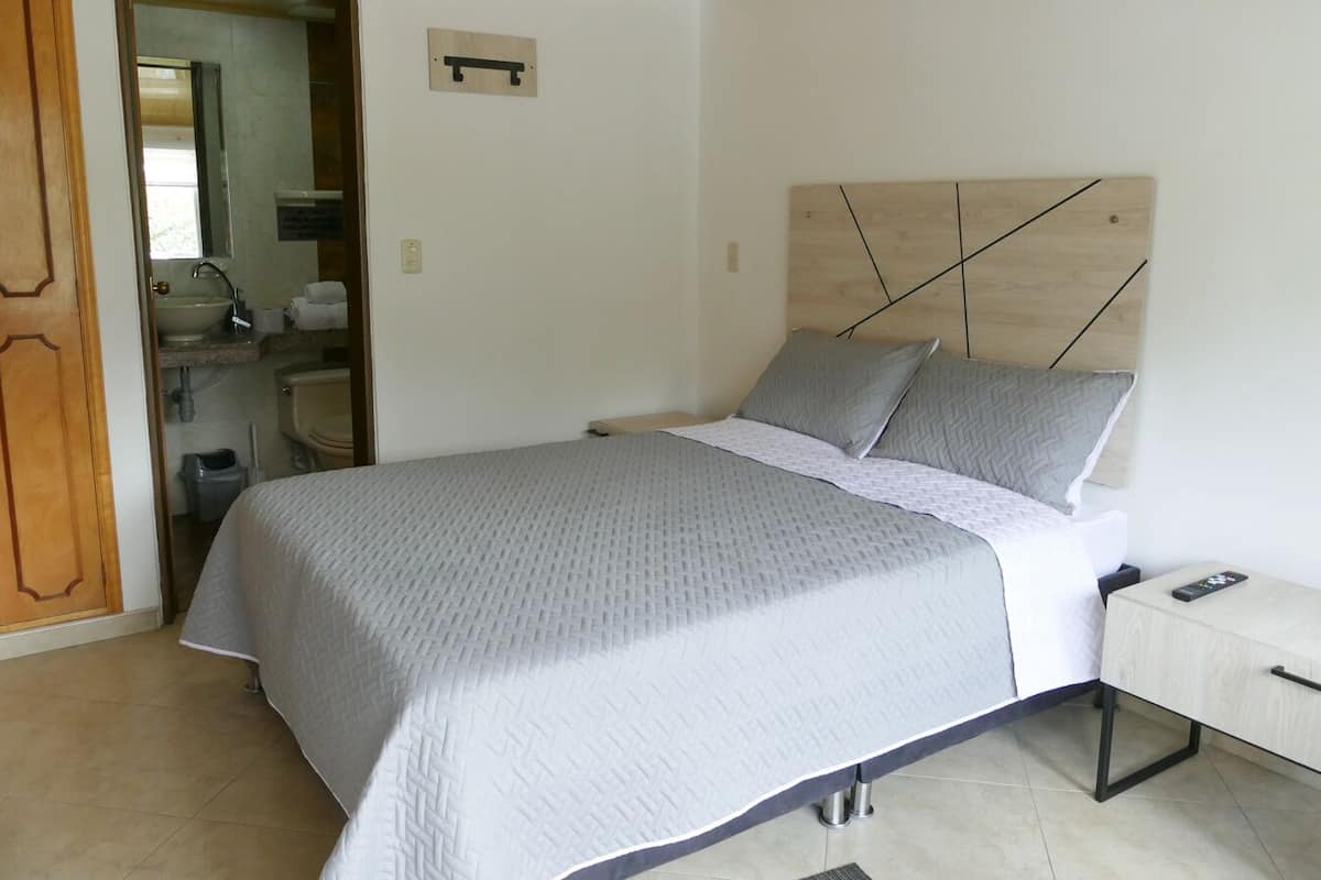 Un dormitorio ordenado con una cama, una mesita de noche y un mueble pequeño.