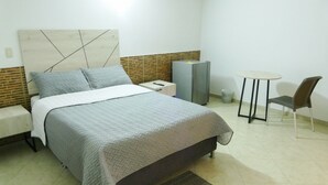 A bedroom with a bed, a nightstand, a chair, a table, and a refrigerator. - BogoRooms Héroes  (Bogotá)
