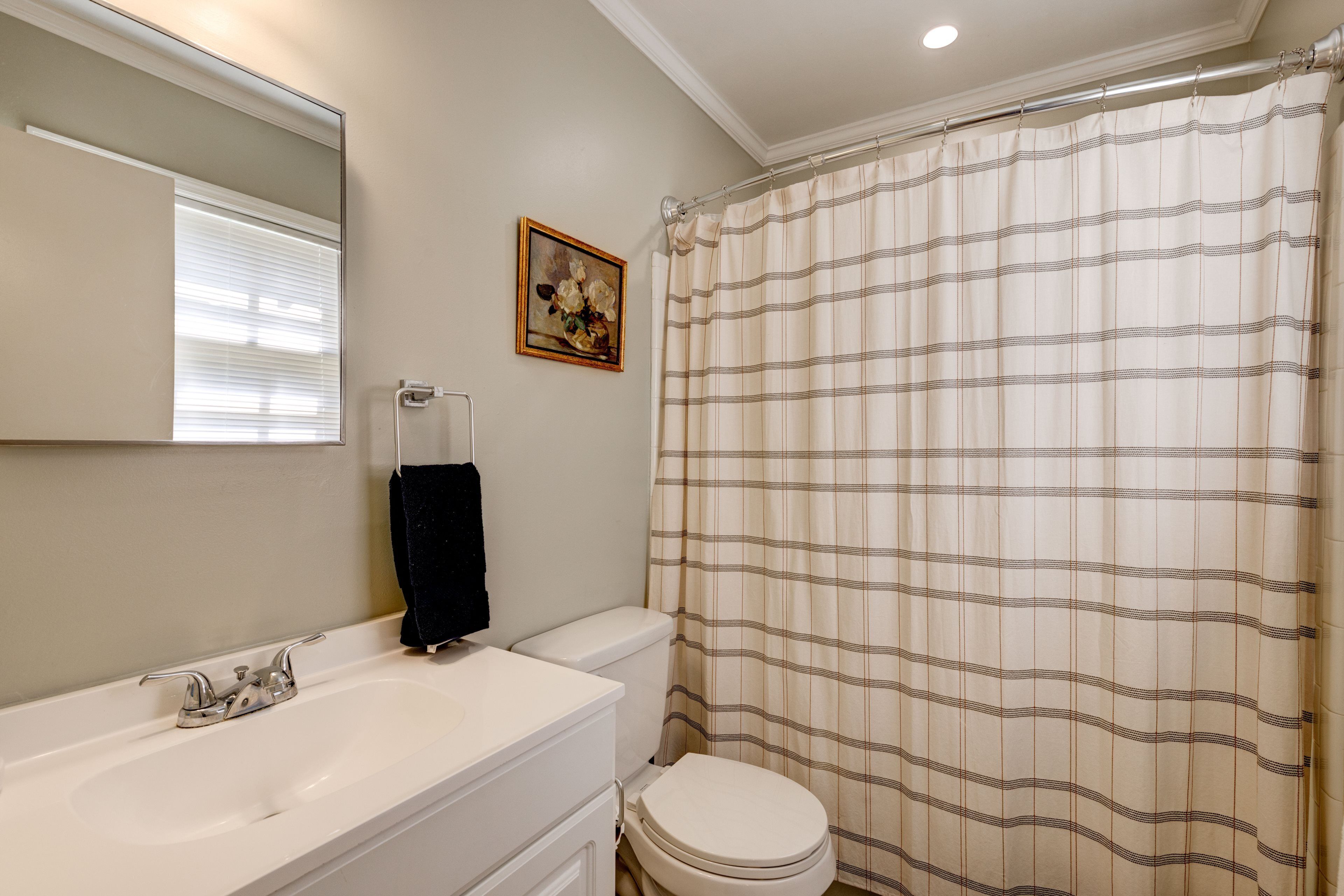 Un baño con lavamanos blanco, espejo, inodoro y cortina de ducha a rayas.