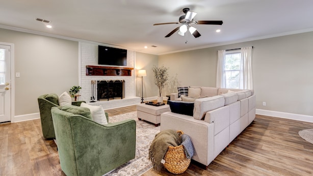 A spacious living room with a fireplace, green armchairs, a white sofa, and a ceiling fan. - Sprawling Updated Ranch with Fireplace on Wimbledon (Thomasville)