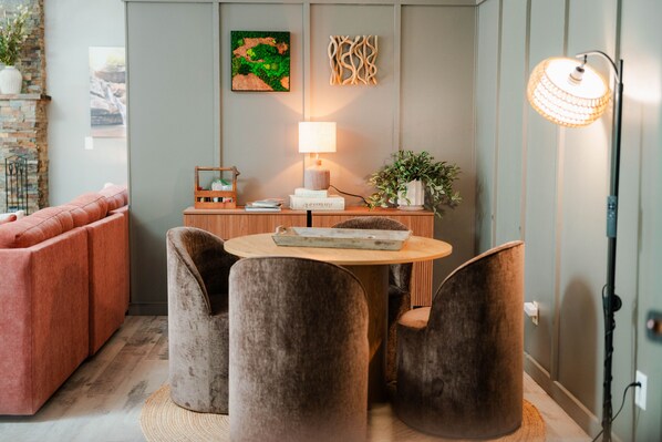 A modern living room with a sofa, a round table with chairs, a lamp, and wall art. - Walnut Hill Lodge | Hocking Hills Luxury, Hot Tub (Logan)