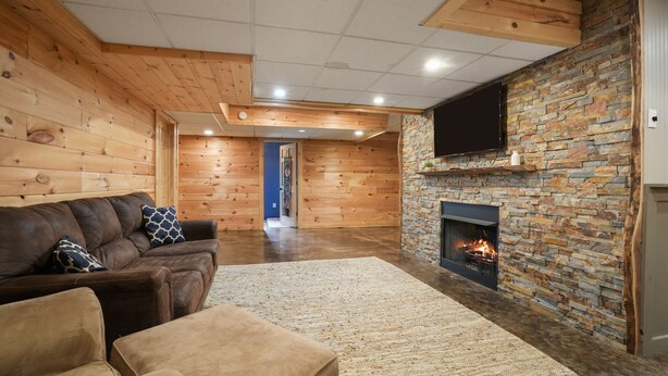 A cozy living room with a stone fireplace, wooden walls, and a flat-screen TV mounted on the wall. - Walnut Hill Lodge  | Hocking Hills Luxury, Hot Tub (Logan)