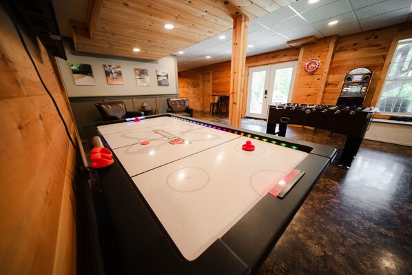Una habitación con mesa de fútbol, mesa de billar y zona de bar con juegos de arcade.