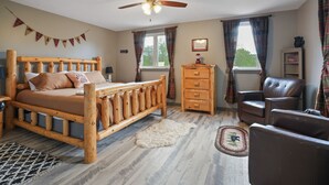A bedroom with a wooden bed, a ceiling fan, a dresser, a chair, and a window with curtains. - Walnut Hill Lodge  | Hocking Hills Luxury, Hot Tub (Logan)