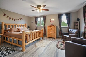 A bedroom with a wooden bed, a ceiling fan, a dresser, a chair, and a window with curtains. - Walnut Hill Lodge | Hocking Hills Luxury, Hot Tub (Logan)