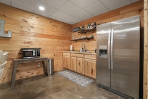 A compact kitchen with wooden walls, a stainless steel refrigerator, a microwave, and a sink.