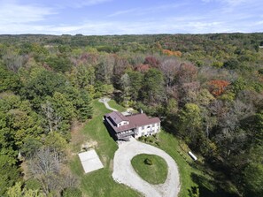 An aerial view of a large, multi-story house surrounded by dense forest, with a well-maintained lawn and a driveway leading to the entrance. - Walnut Hill Lodge | Hocking Hills Luxury, Hot Tub (Logan)
