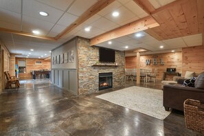 A spacious living area with a stone fireplace, wooden ceiling beams, and a flat-screen TV mounted on the wall.