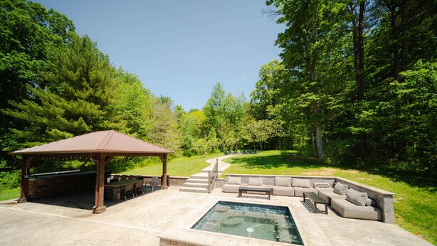 A covered outdoor area with a barbecue, seating, and a hot tub. - Walnut Hill Lodge  | Hocking Hills Luxury, Hot Tub (Logan)