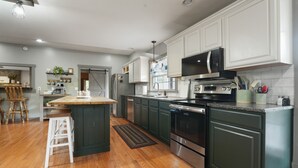 A modern kitchen with white cabinets, a central island, stainless steel appliances, and a wooden floor. - Walnut Hill Lodge  | Hocking Hills Luxury, Hot Tub (Logan)