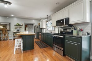 A modern kitchen with white cabinets, a central island, stainless steel appliances, and a wooden floor.