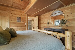 A wooden cabin interior with a bed, a mirror, and a sign that reads "Like Better at the Cabin."