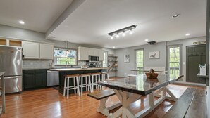 A modern kitchen with a central island, wooden flooring, and white cabinetry. - Walnut Hill Lodge  | Hocking Hills Luxury, Hot Tub (Logan)