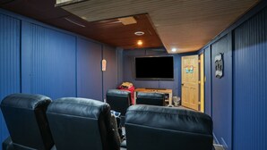 A home theater room with blue walls, a wooden ceiling, and black leather seating. - Walnut Hill Lodge  | Hocking Hills Luxury, Hot Tub (Logan)