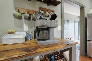 A kitchen with a coffee maker, mugs on a wall, a wooden table, and a refrigerator. - Walnut Hill Lodge | Hocking Hills Luxury, Hot Tub (Logan)