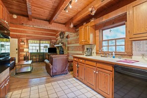Une cuisine chaleureuse, aménagée dans le style d’un chalet, avec des meubles en bois, un coin repas comprenant une table et des chaises, et une grande fenêtre décorée d’une étoile.