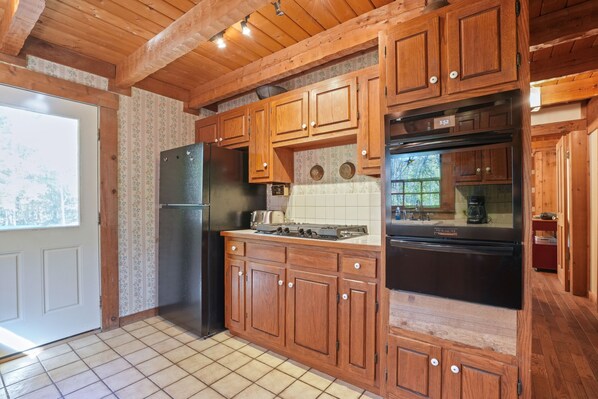 Una cocina con armarios de madera, un refrigerador negro, una estufa y un horno negro.