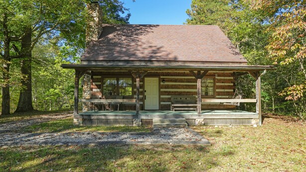 A rustic log cabin with a porch, a stone fireplace, and a bench.