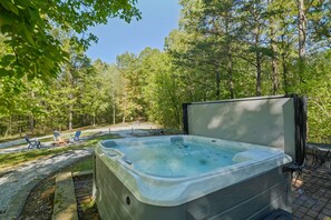 A hot tub in a wooded area with a fire pit and outdoor seating.