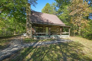 A rustic log cabin with a porch, surrounded by trees.