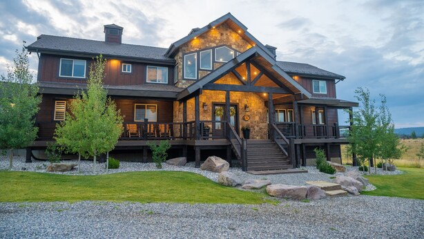 A large, multi-story house with a prominent stone facade, multiple windows, and a well-maintained lawn with rocks and trees. - All-Season Luxury MTN Retreat @ Lake w/ Hot Tub, Sauna & Near Hiking Trails, YNP (Island Park)
