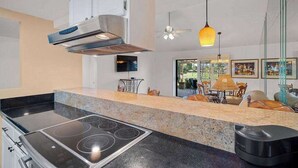 Cozinha moderna com fogão embutido, armários brancos e uma grande janela com vista para um jardim.