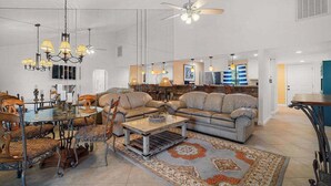 Uma sala de estar espaçosa com um sofá grande, uma mesa de centro de vidro e um espaço de jantar com um candelabro.