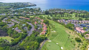 Vista aérea de un complejo turístico costero con un campo de golf, propiedades frente a la playa y un gran hotel.