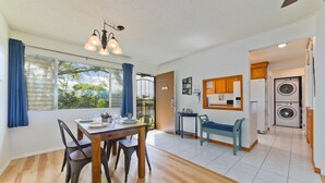Amplia sala de estar con mesa de comedor, sillas, un banco, lavadora y zona de cocina.