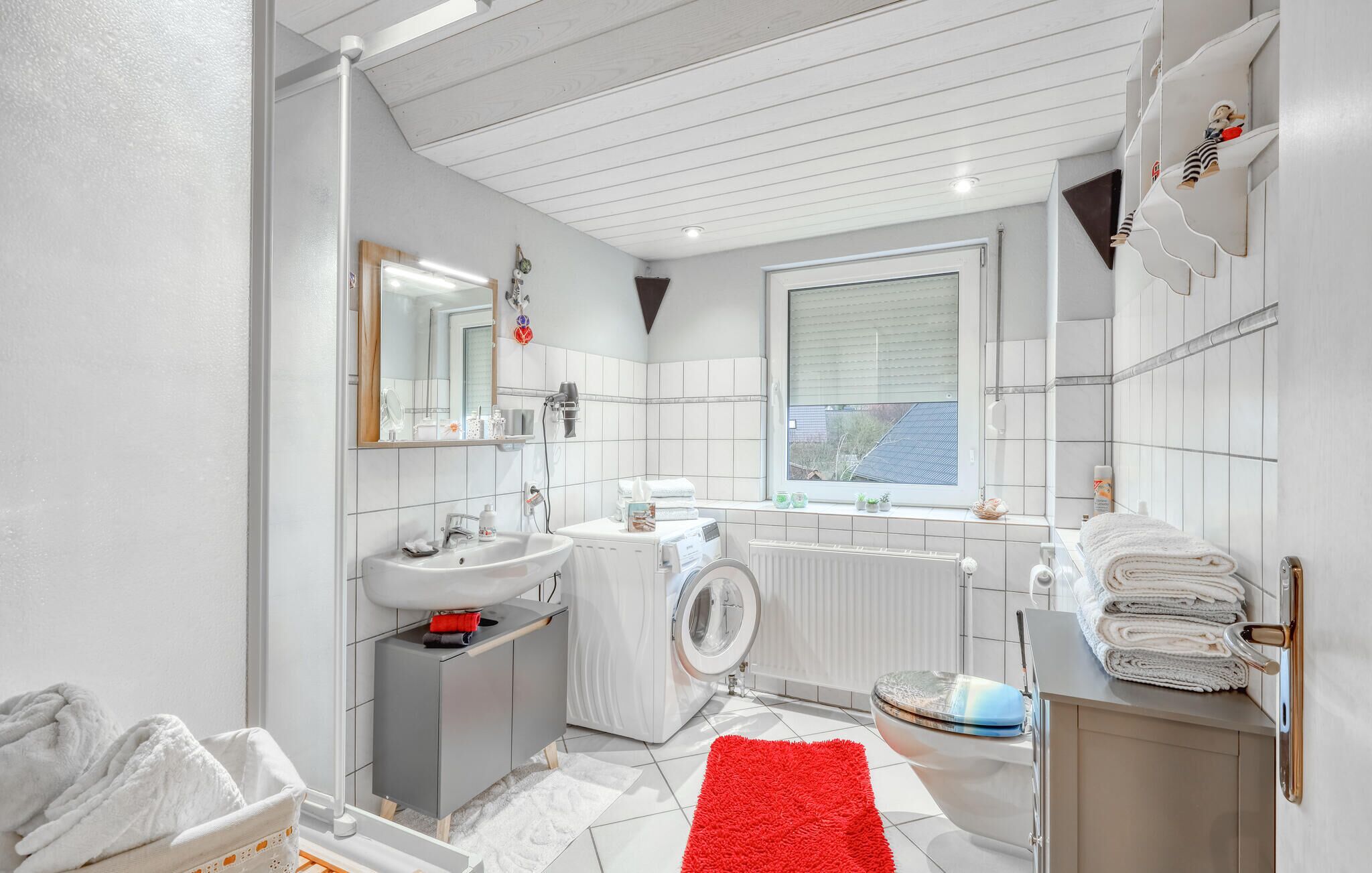 A modern bathroom with a sink, mirror, towel rack, and a window.