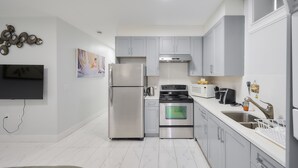 A modern kitchen with stainless steel appliances, grey cabinets, and a flat-screen TV mounted on the wall. - Basement Suite in Vancouver (Vancouver)