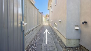 A narrow alleyway with a paved path, flanked by buildings with metal siding and a beige wall. - Basement Suite in Vancouver (Vancouver)