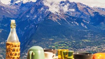 Ein Tisch mit Flasche, Tasse und Bechern vor einer Berglandschaft.