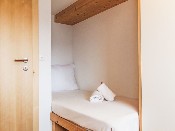 A small, single-bed room with a wooden ceiling beam, a white wall, and a door with a keyhole. - Le mayen des Veillas by Interhome (Nendaz)
