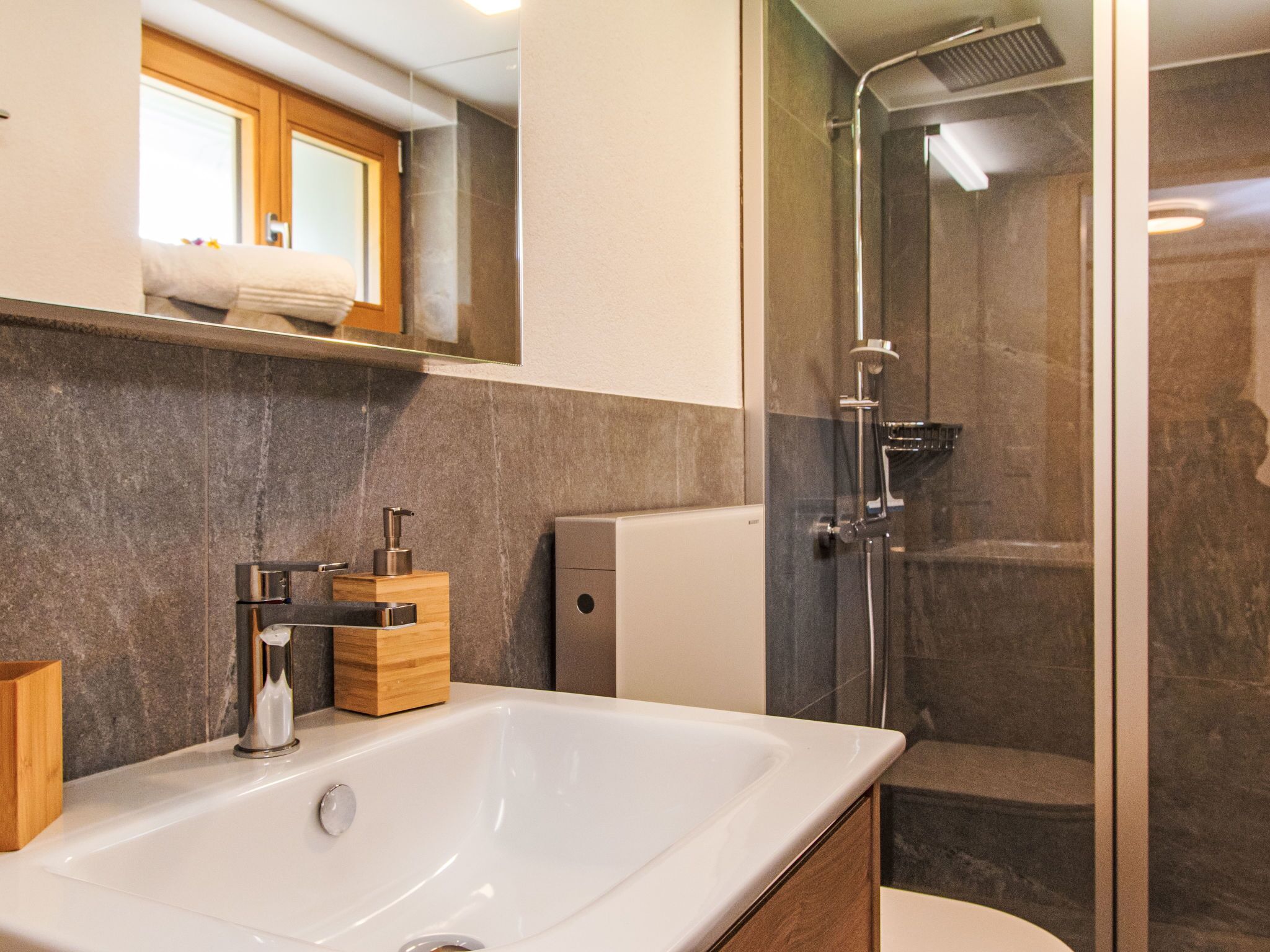 A modern bathroom with a large white sink, a glass shower enclosure, and a wooden vanity.