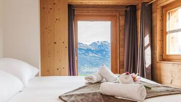 Ein Zimmer in einer Holzhütte mit einem Bett, Bergblick und einem Fenster mit Vorhängen.